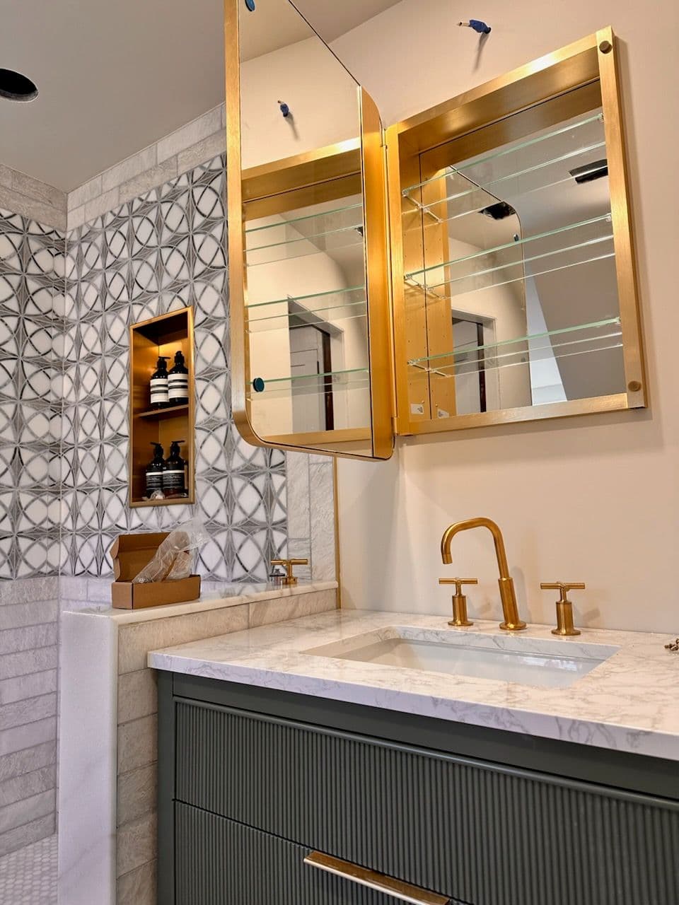 Modern bathroom design featuring a gold faucet, elegant mirror, and patterned wall tiles.