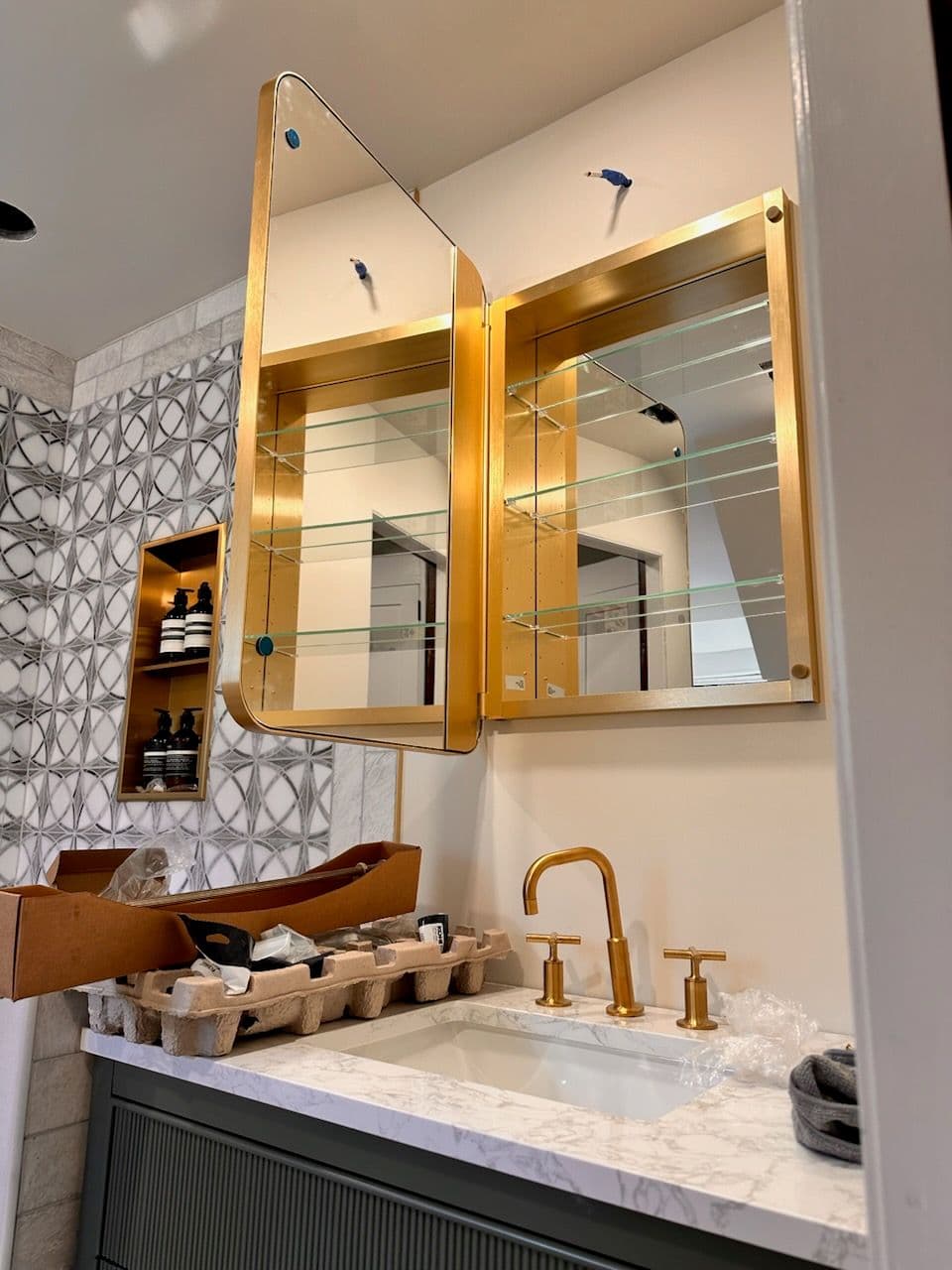 Modern bathroom with golden mirror, sink faucet, and decorative tiles.