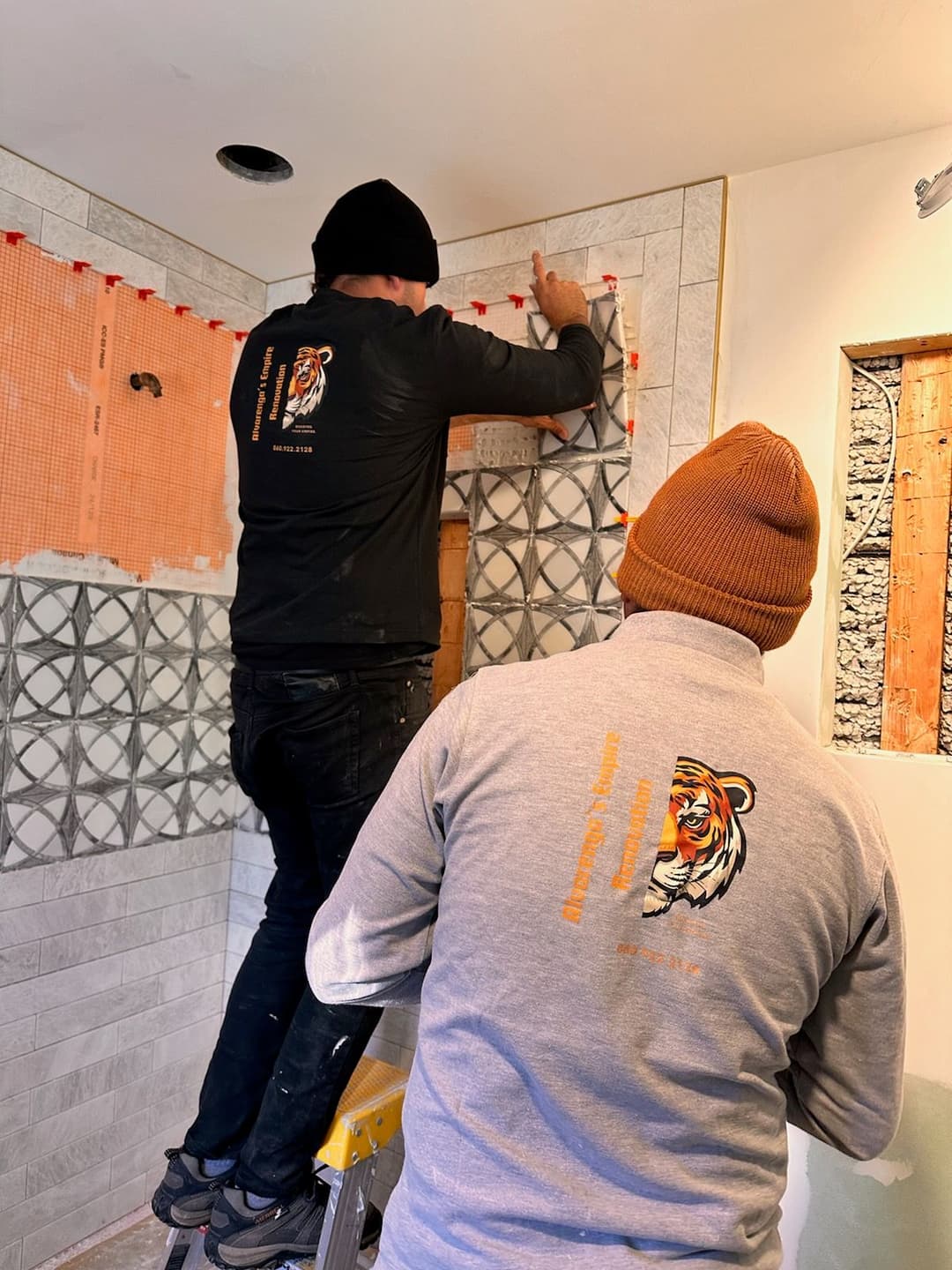 Workers installing decorative tile in a bathroom renovation project.