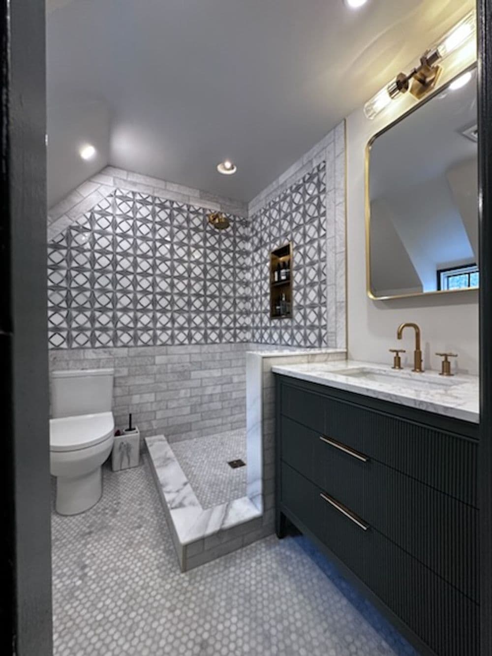 Modern bathroom with geometric tile, marble accents, gold fixtures, and dark cabinetry.