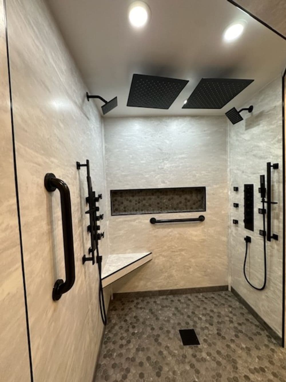 Modern accessible shower with dual rain showerheads, grab bars, and stylish stone accents.