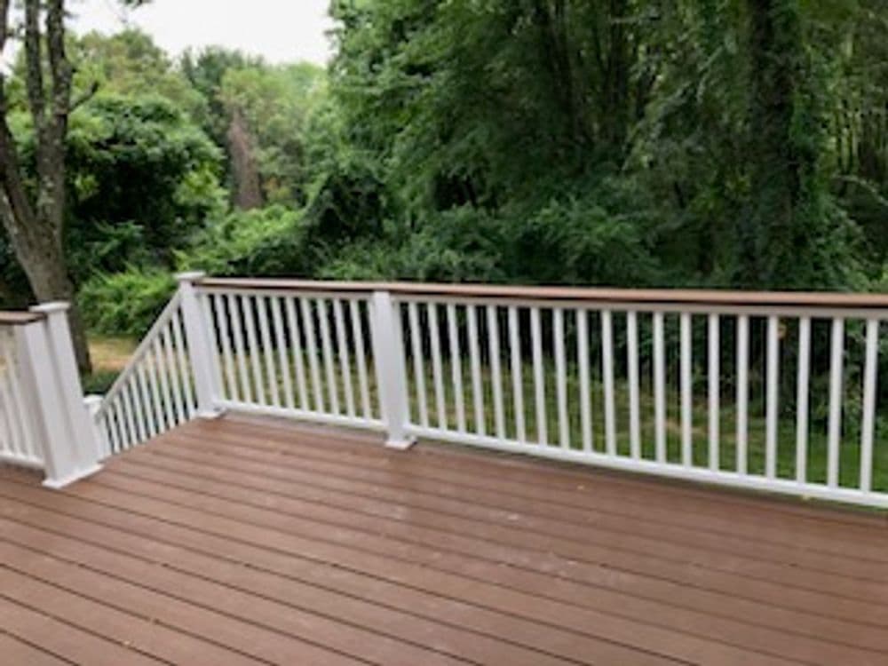 White railing on a wooden deck overlooking a lush green landscape.