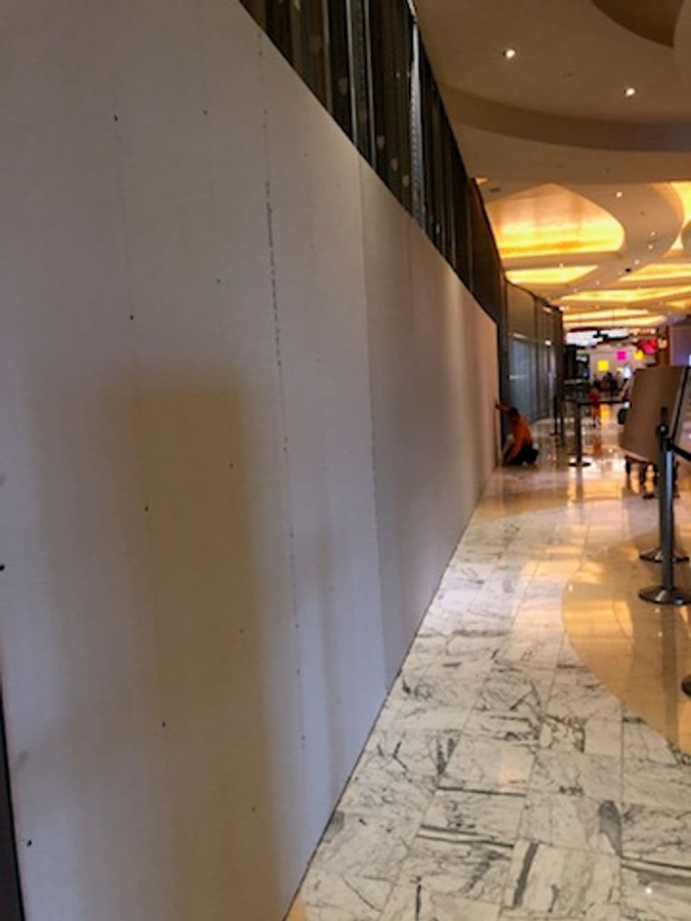 Construction wall in a mall corridor with marble floors and soft lighting.