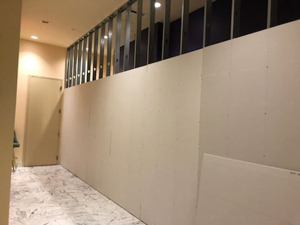 Interior construction view showing drywall installation in a hallway with marble flooring.
