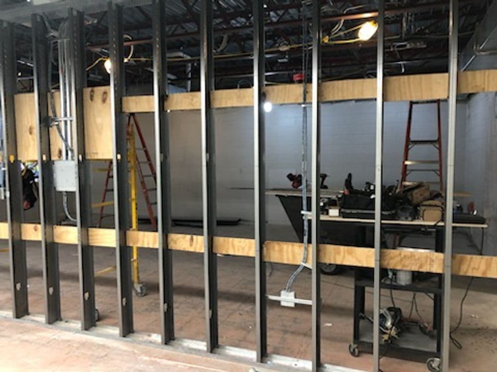Framed wall under construction with ladders and tools visible in a commercial space.