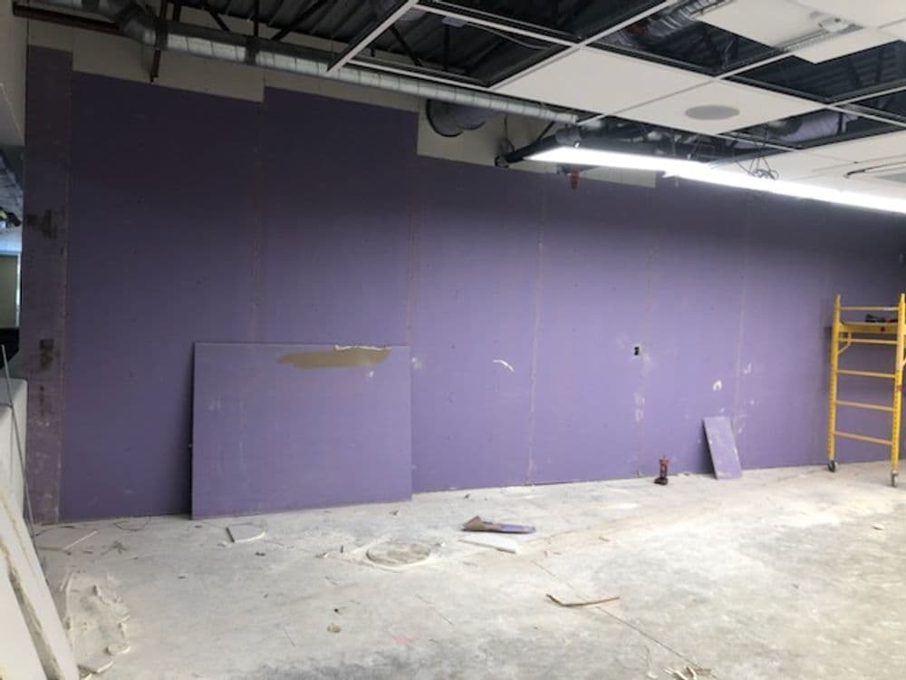 Interior construction site with unfinished purple drywall and tools scattered on the floor.